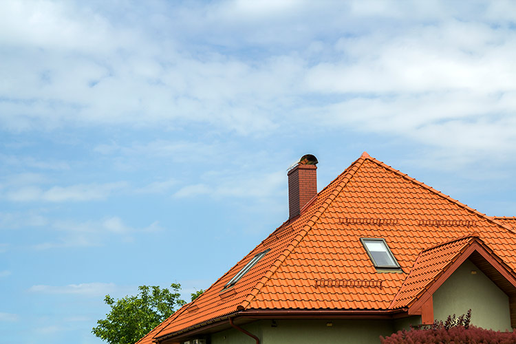 close up detail new modern house top with shingled red roof high chimney attic windows clear blue sky